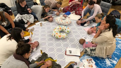 Infant massage training class with parents, babies and demonstration dolls participating in a family-centred group session