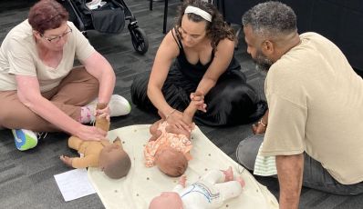 Parents learning baby massage with guidance from a student demonstrating techniques on a doll during Brisbane training