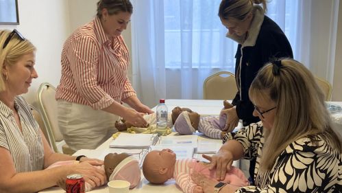 Students participating in practical infant massage training with demonstration dolls and course materials